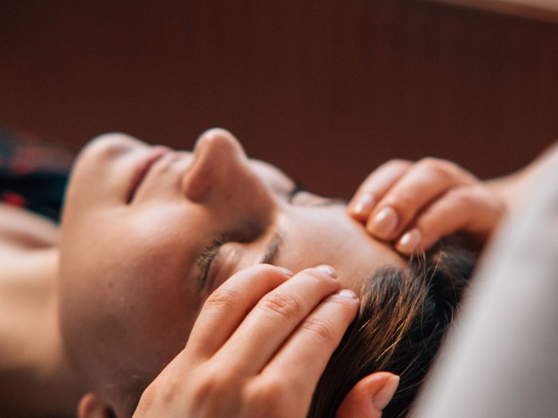 Head Spa Massage: beide Hände massieren Schläfen und Kopfhaut einer liegenden Person