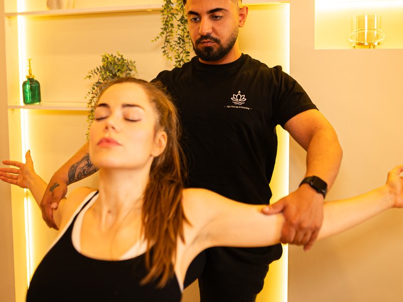 Assistiertes Stretching: Trainer dehnt Schultern und Arme einer Kundin im Stehen